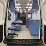 Standing outside Sprinter mobile medical clinic looking at cabinets, bed, sink, and stool