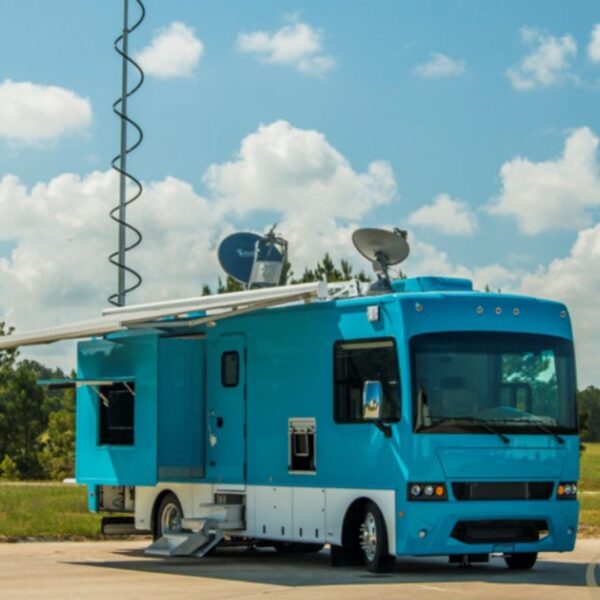 A bright blue mobile command unit with satellite dishes and an extended communications mast ready for deployment.